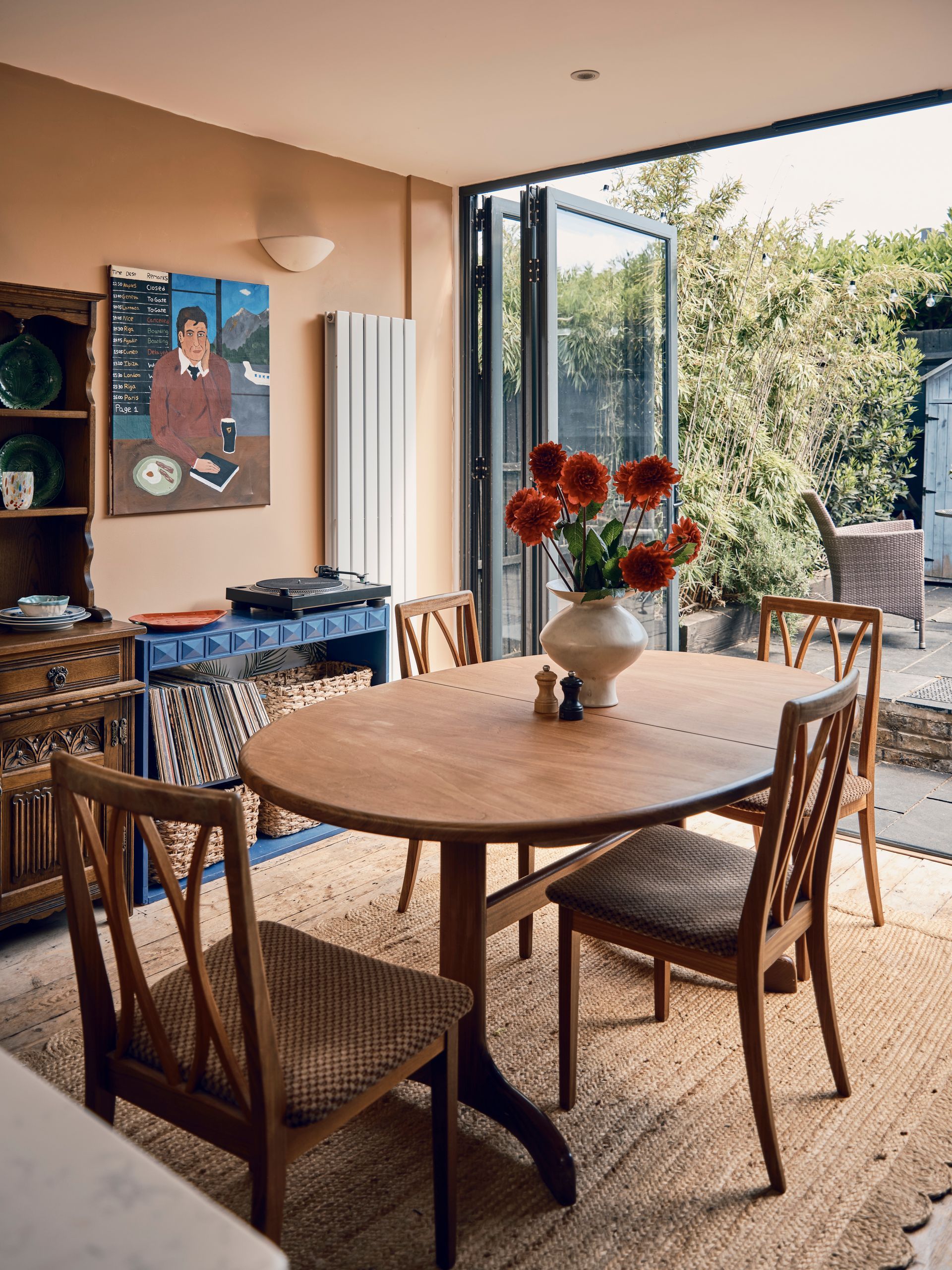 Round wooden dining table with red dahlias beside bi-fold doors opening onto a bamboo-lined patio