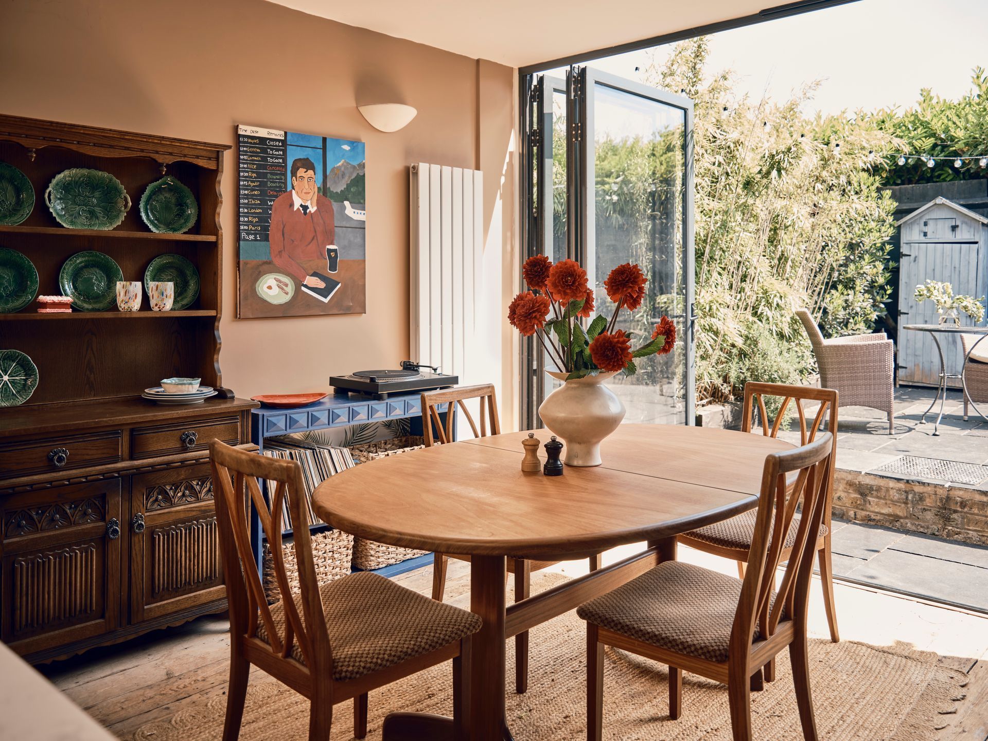 Dining room designed by Heather Brazier with an antique oak dresser, folk-art painting and bi-fold doors opening onto a garden