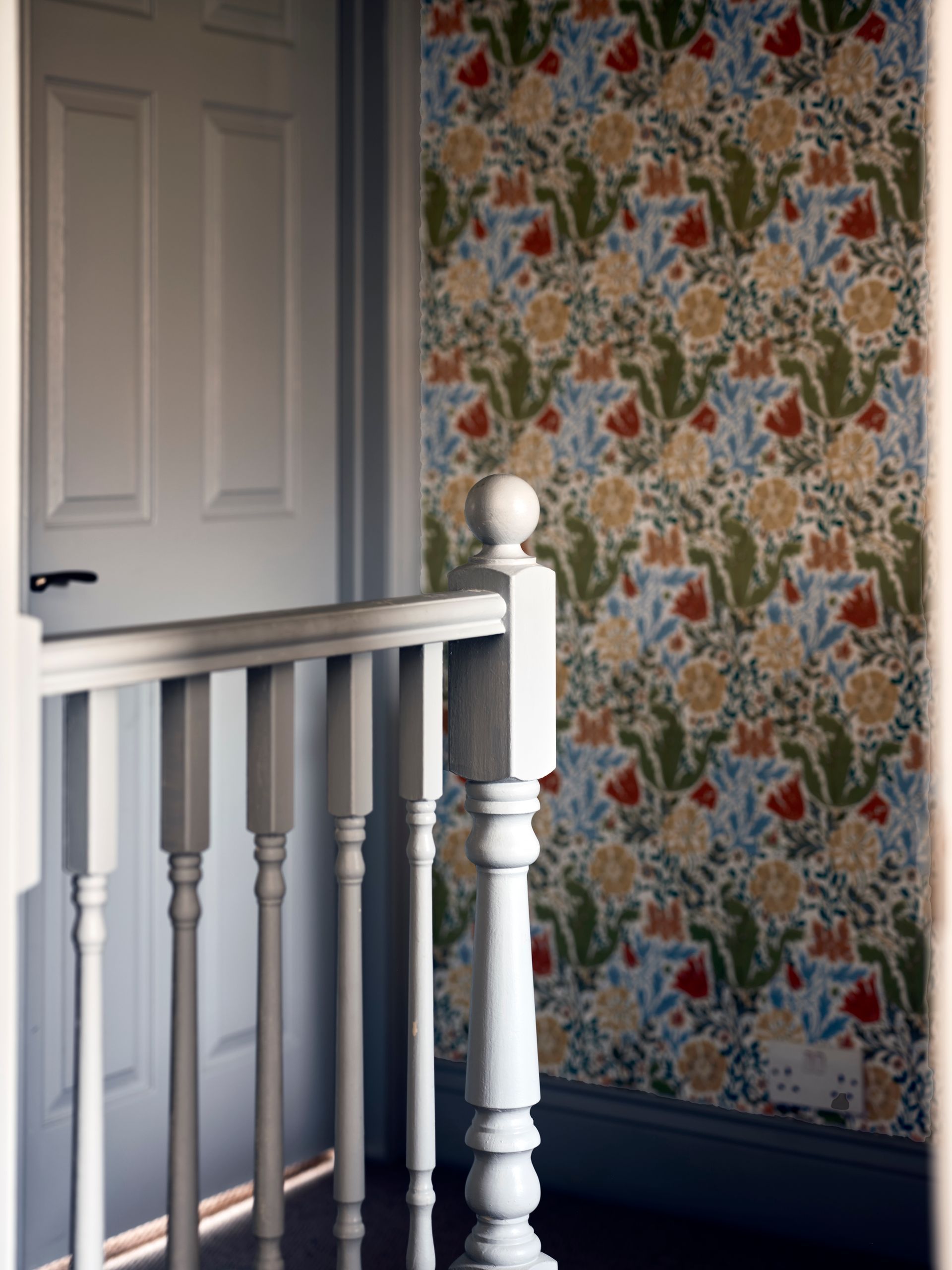Hallway landing with a grey-painted banister against richly patterned floral wallpaper