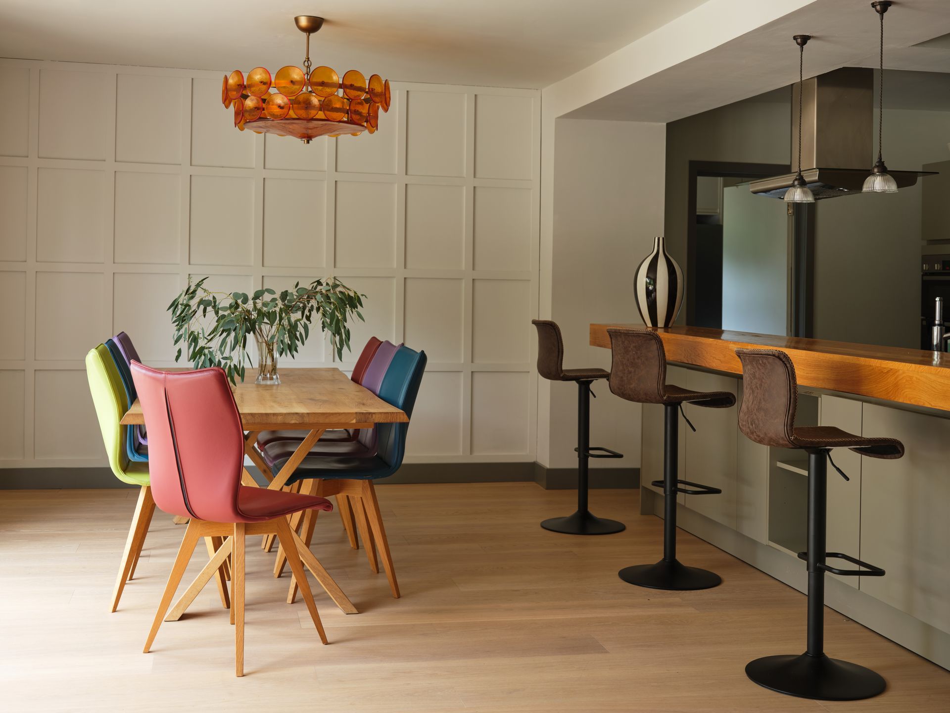 Dining space with bespoke leather chairs in pink, green, blue and purple beneath an amber glass chandelier