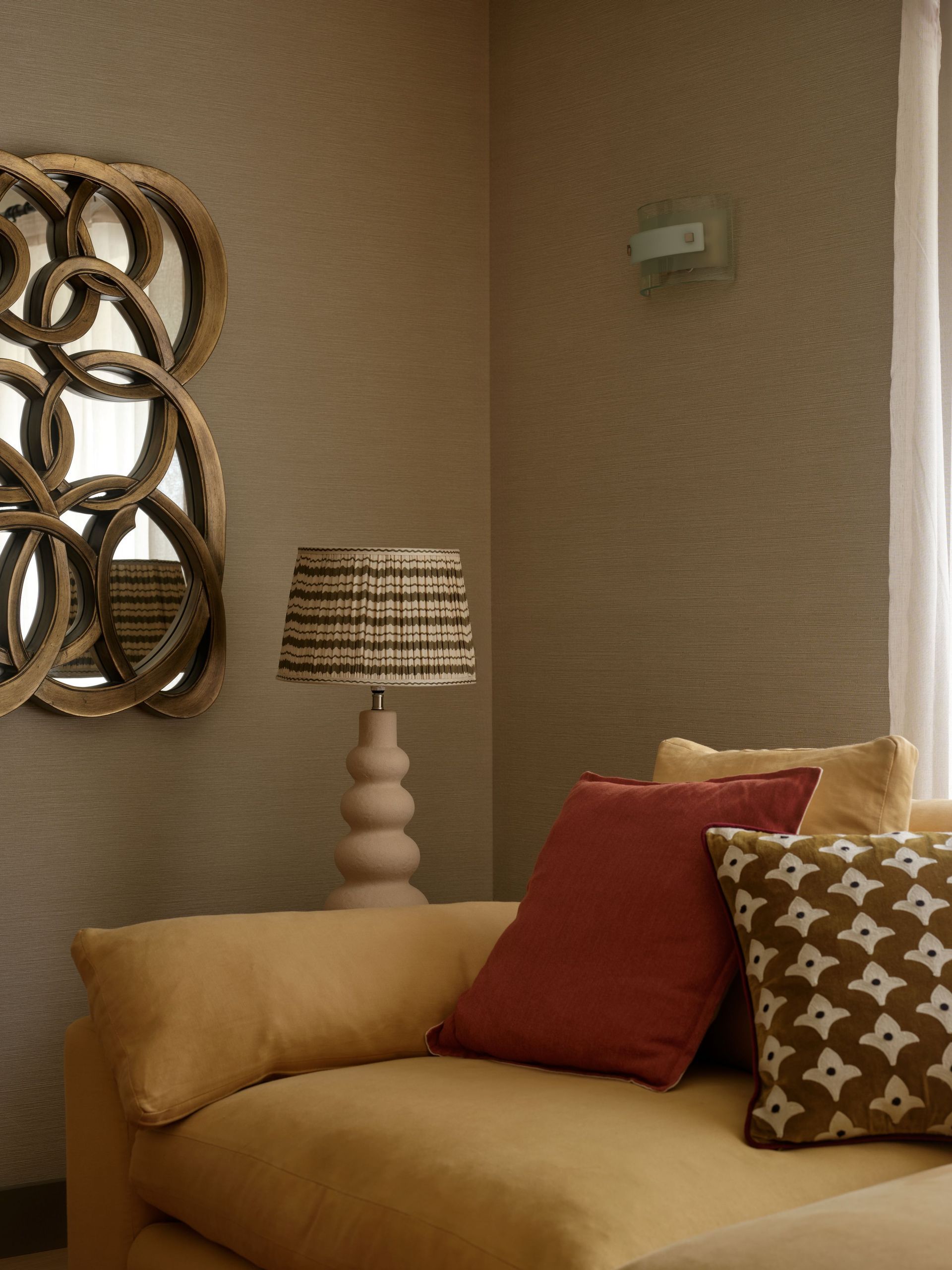 Living room corner with a gold interlocking-circles mirror, sculptural cream lamp and mustard sofa