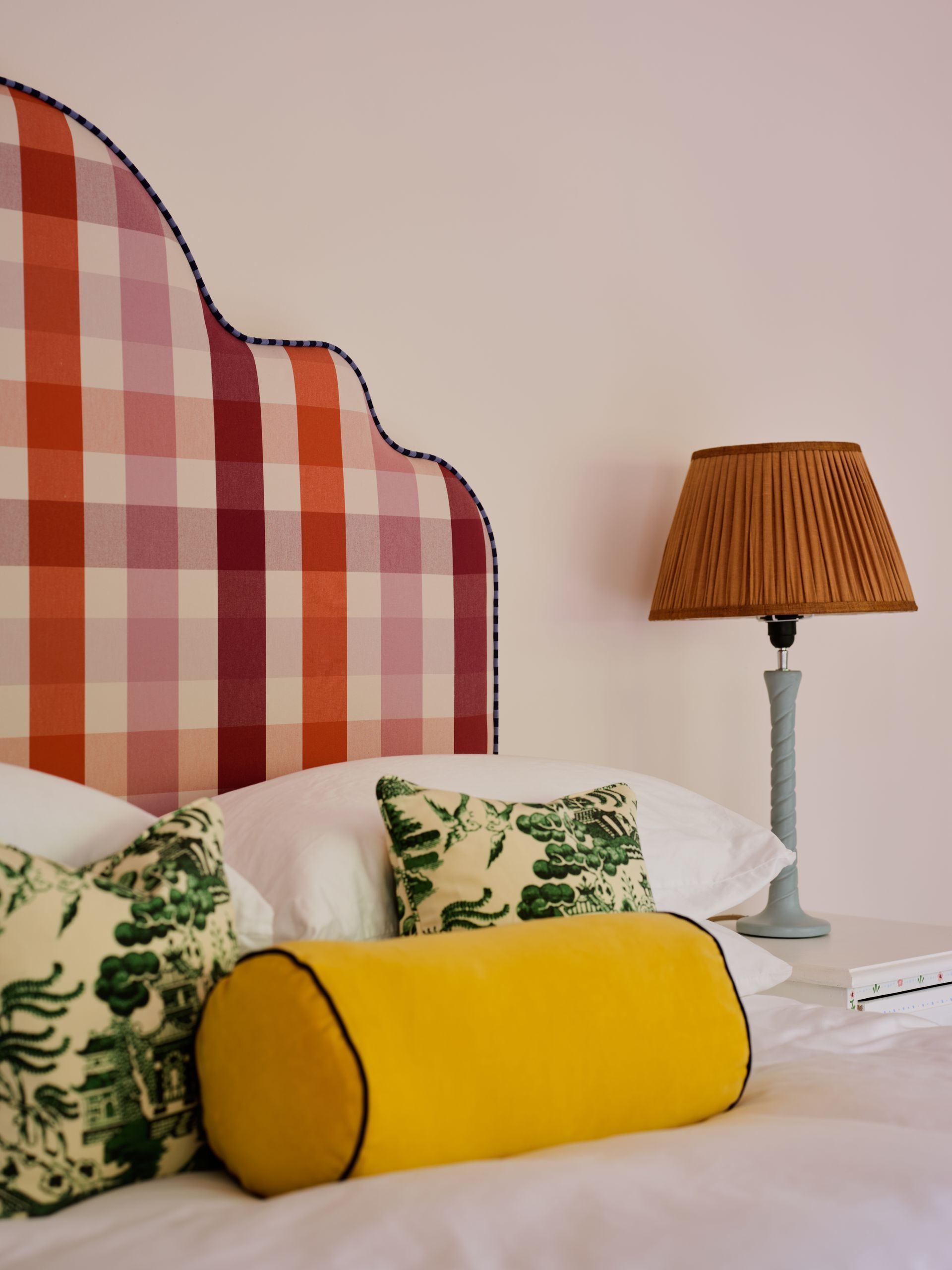 Bedroom with a scalloped headboard in orange and pink check and green chinoiserie cushions