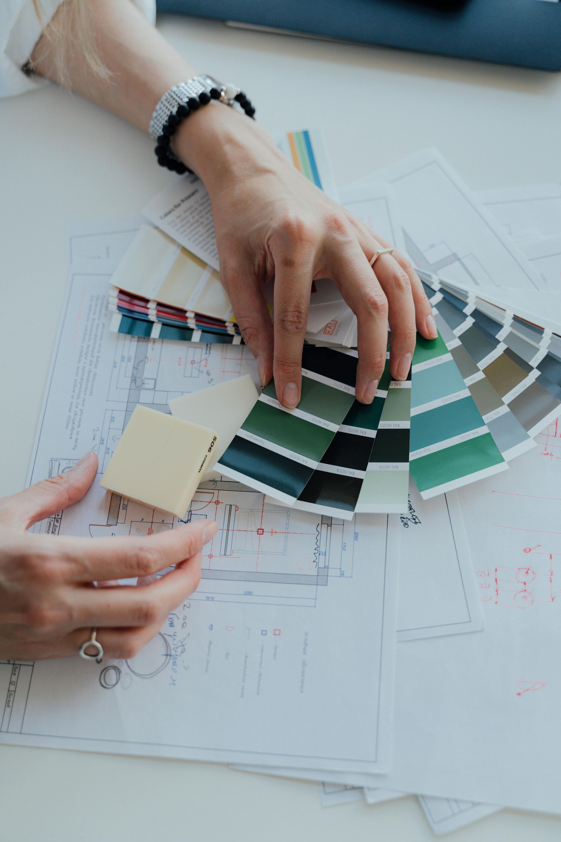 Designer’s hands fanning out colour swatches over floor plans during an interior design consultation
