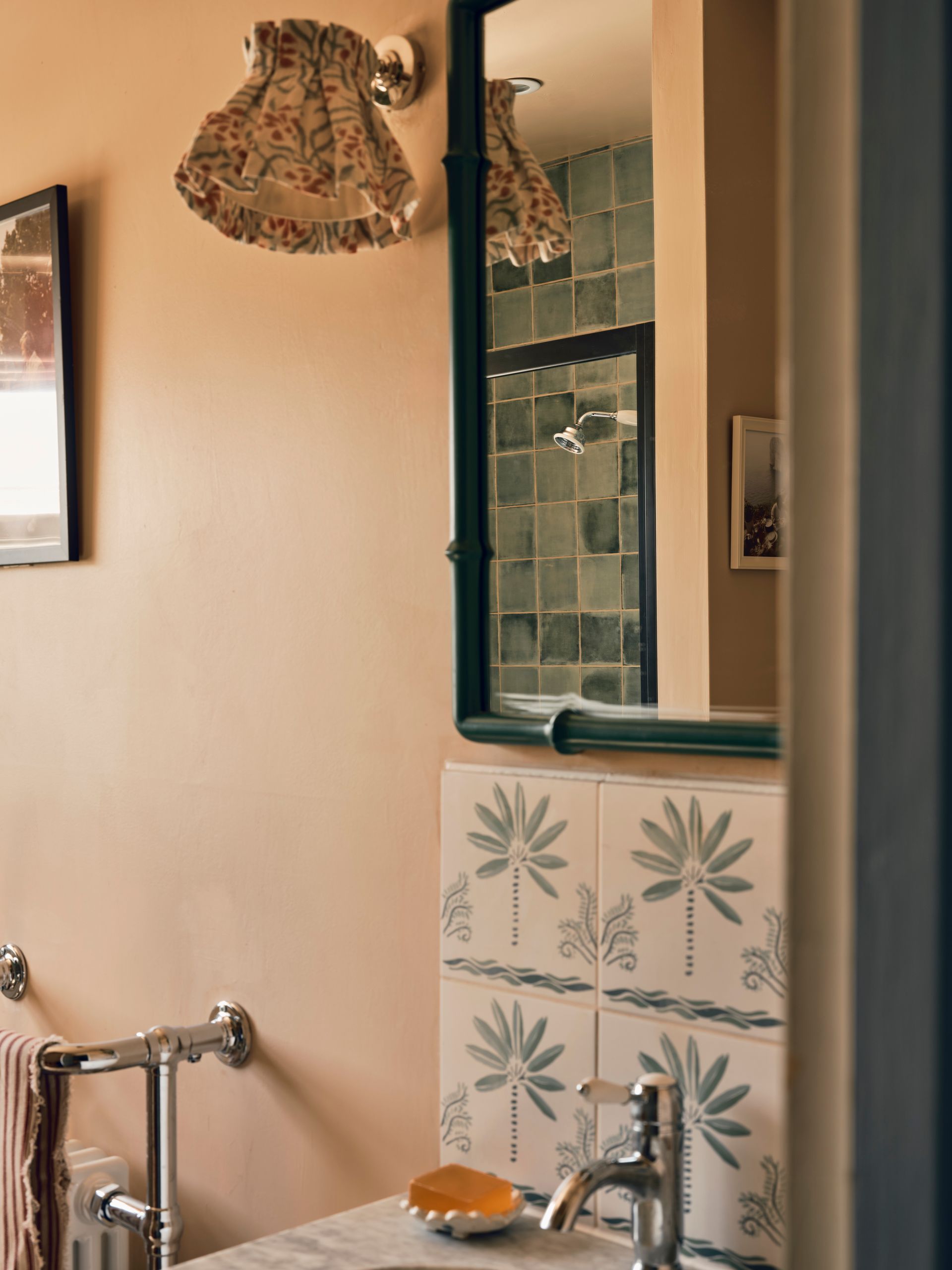 Bathroom with palm-motif tiles, a dark green bamboo-style mirror and green-tiled shower reflected within it